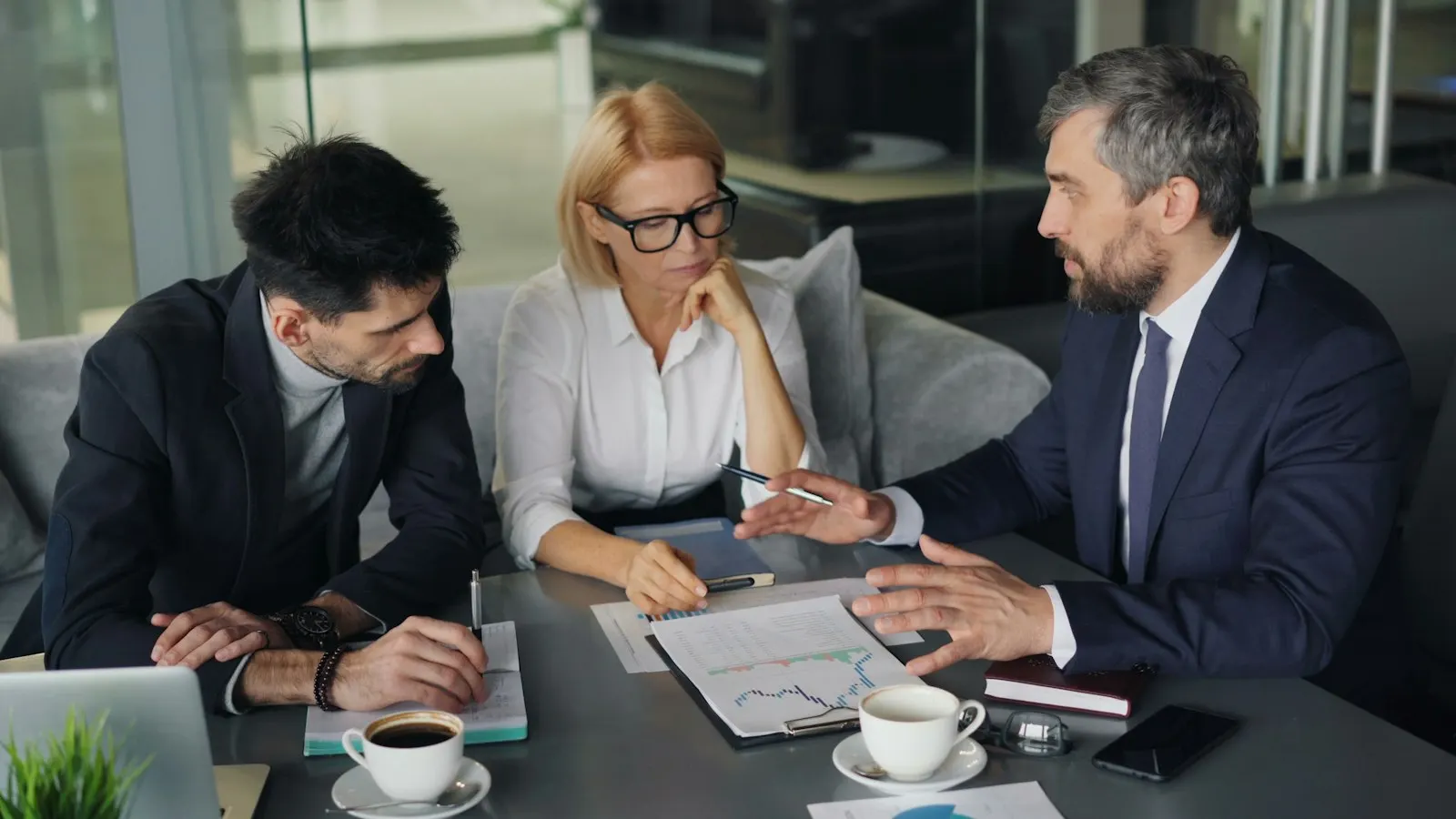 Three people talking through plans and figures around a table
